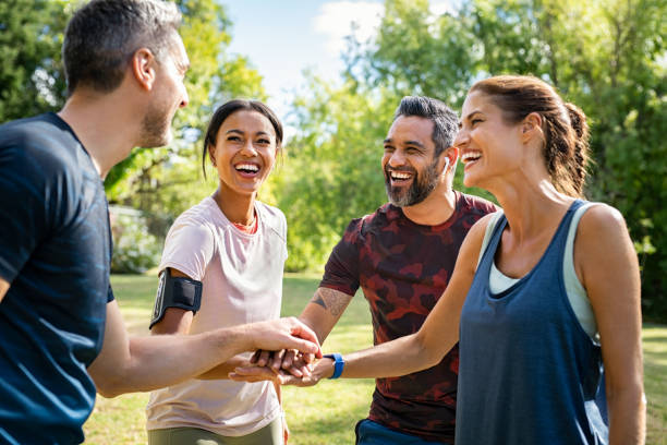 Group of active mature friends in park stacking hands after workout Laughing mature and multiethnic sports people putting hands together at park. Happy group of men and beautiful women smiling and stacking hands outdoor after fitness training. Multiethnic sweaty team cheering after intense training. exercise class photos stock pictures, royalty-free photos & images