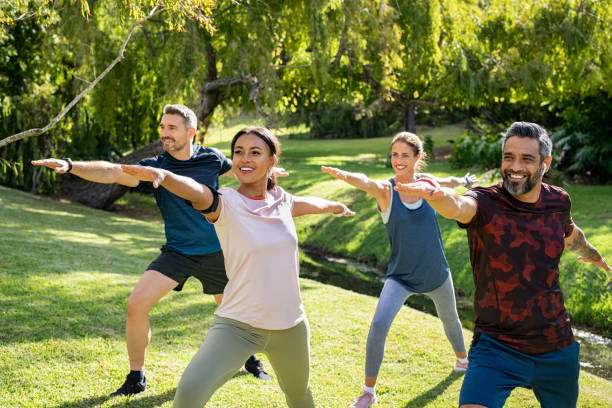 gruppo di uomini e donne maturi che si allungano al parco dopo l'allenamento - yoga exercising outdoors group of people foto e immagini stock