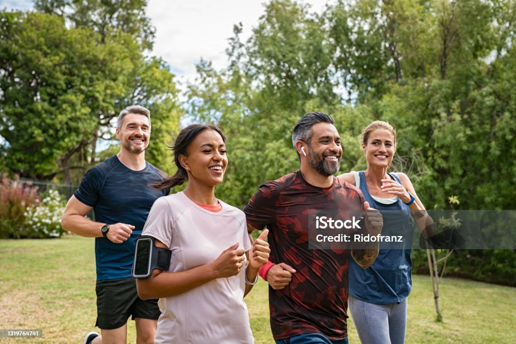 Mature people jogging in park Healthy group of multiethnic middle aged men and women jogging at park. Happy mixed race couples running together. Mature friends running together outdoor. Exercising Stock Photo