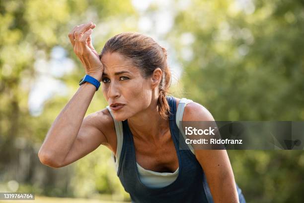 Tired Mature Runner Wiping Sweat After Workout At Park Stock Photo - Download Image Now