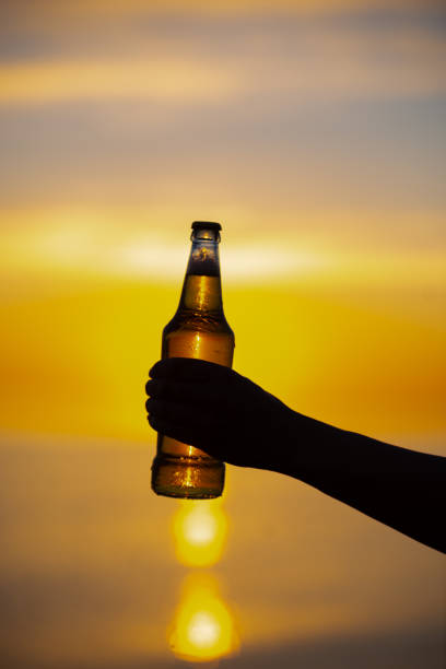 les femmes tenant une bouteille de bière sur le thème du midsummer dans leurs mains au coucher du soleil. bouteille de bière lumière dorée du soleil, formant des bulles bokeh. faible profondeur de champ - shadow focus on shadow women sunset photos et images de collection