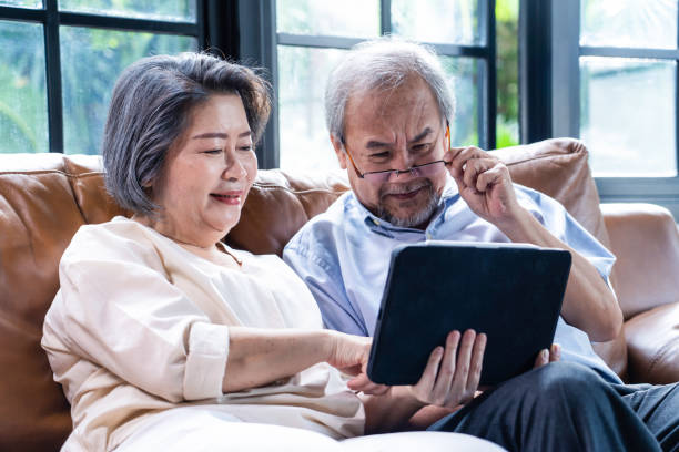 kochający asian senior starsza kobieta i starzec para siedzieć na kanapie w salonie używać laptopa do czytania wiadomości i rozmowy wideo online z rodziną w domu. dziadkowie czują się zadowoleni z komunikacji przez internet - two parent family asian ethnicity couple computer zdjęcia i obrazy z banku zdjęć