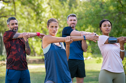 Mature woman and middle aged man stretching at park. Mid adult multiethnic group working out in park doing stretching exercise. Healthy group of mixed race friends doing stretching exercises together.
