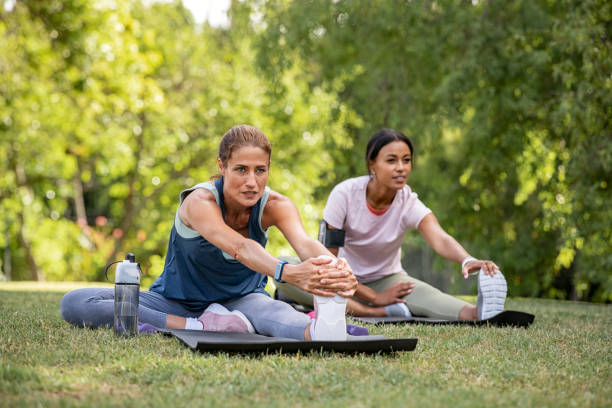 dwie kobiety wykonujące ćwiczenia rozciągające w parku - yoga flexibility two people women zdjęcia i obrazy z banku zdjęć