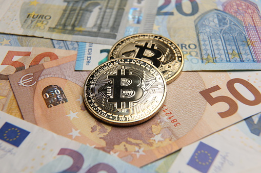 London, UK - 05 22 2021: Bitcoin coins cryptocurrency on Euro money banknotes background.