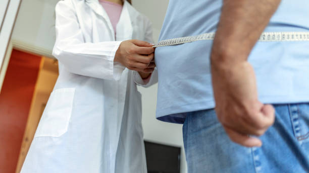 栄養士の医師は、脂肪組織と過剰体重の測定テープを持つ男性患者の体を測定します。 - mature adult sadness overweight women ストックフォトと画像