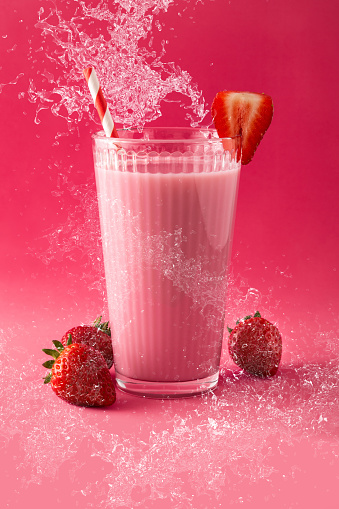 Strawberry milkshake splashing in glass on pink background