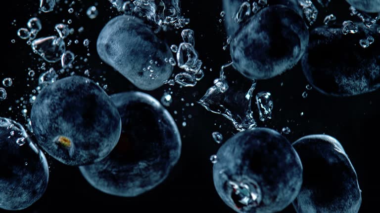 SLO MO LD Blueberries falling into water against black background