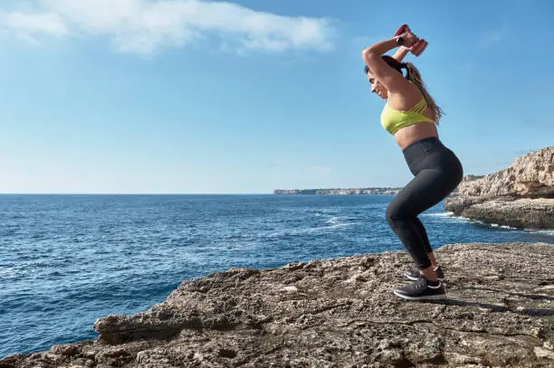 Latin woman, middle-aged, wearing sportswear, training, doing physical exercises, plank, sit-ups, climber's step, burning calories, keeping fit, outdoors by the sea, wearing headphones, smart watch