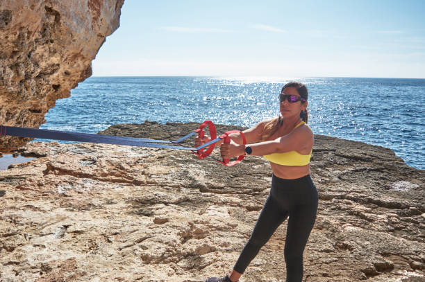 mulher latina, de meia-idade, usando roupas esportivas, treinando, fazendo exercícios físicos, prancha, abdominais, passo do alpinista, queima de calorias, manutenção de forma, ao ar livre à beira-mar, usando fones de ouvido, relógio inteligente - pilates women sit ups yoga - fotografias e filmes do acervo