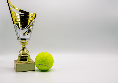A tennis trophy and tennis ball composition in yellow and golden tones with copy space
