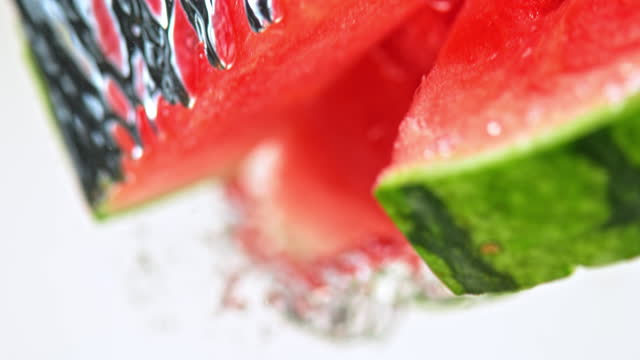 SLO MO LD Watermelon slices falling into water against white background