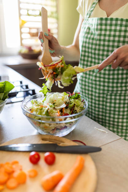 Close up of woman mixing fresh salad for lunch in the kitchen