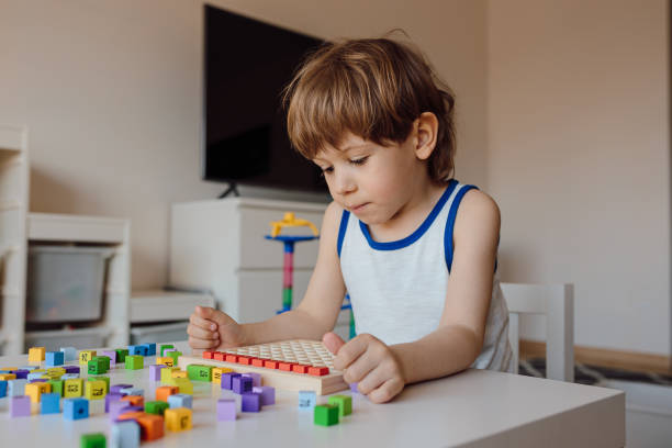 menino de 3 anos está imerso em seu próprio mundo. obsessão infantil com números e contagem. manifestação do autismo em crianças. - autismo - fotografias e filmes do acervo