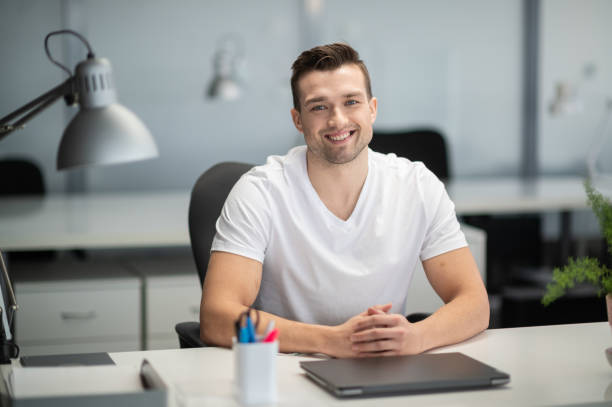 A young manager sits at a desk in the office and smiles for a photo stock photo