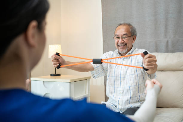 istock Asian Disabled senior elderly man sitting on sofa doing physiotherapist with support from therapist nurse. Older handicapped man using resistance stretch band exercise for patient in home nursing care 1319783128