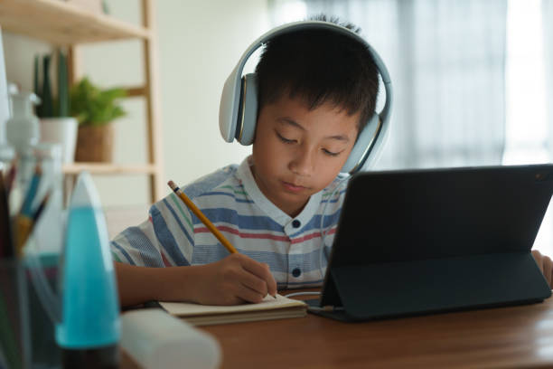 istock Asian boy learning online via internet with a tutor on a tablet digital with headphone, Asia child is studying while sitting in the living room at home. Concept of online learning at home 1319783329