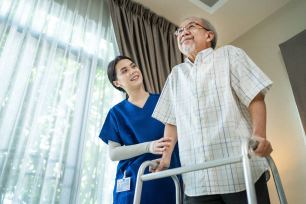 paciente discapacitado de edad avanzada asiática caminando lentamente con caminante en la atención del hogar de ancianos. la enfermera terapeuta del cuidador apoya el uso masculino discapacitado más viejo zimmer marco. concepto de seguro de terapia méd - home health nurse fotografías e imágenes de stock