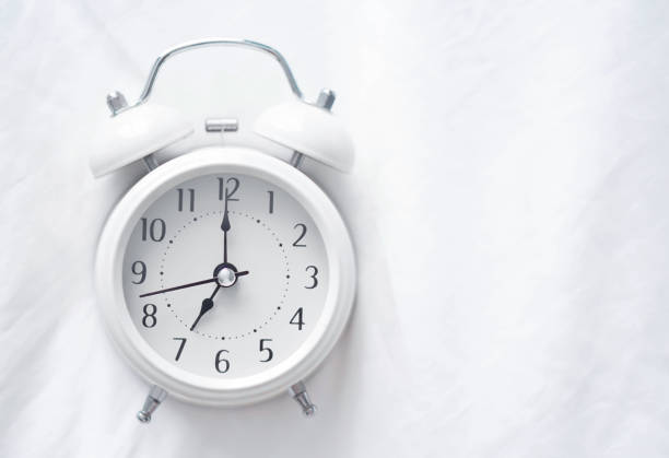 istock Close up top view Alarm clock on white bad with light from window, selective focus 1319783792