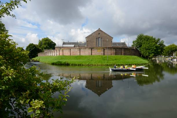 Utrecht, the Netherlands - August 13, 2017: Wolvenplein Penitentiary was built in 1856. The former prison is now a breeding ground for creativity and other initiatives, like a restaurant and an escape room. The building is situated along a moat that surrounds the city centre. On the water a rowboat is passing by.