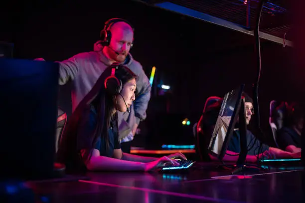 Photo of Esports team training camp in computer club with coach, caucasian guy and asian girl