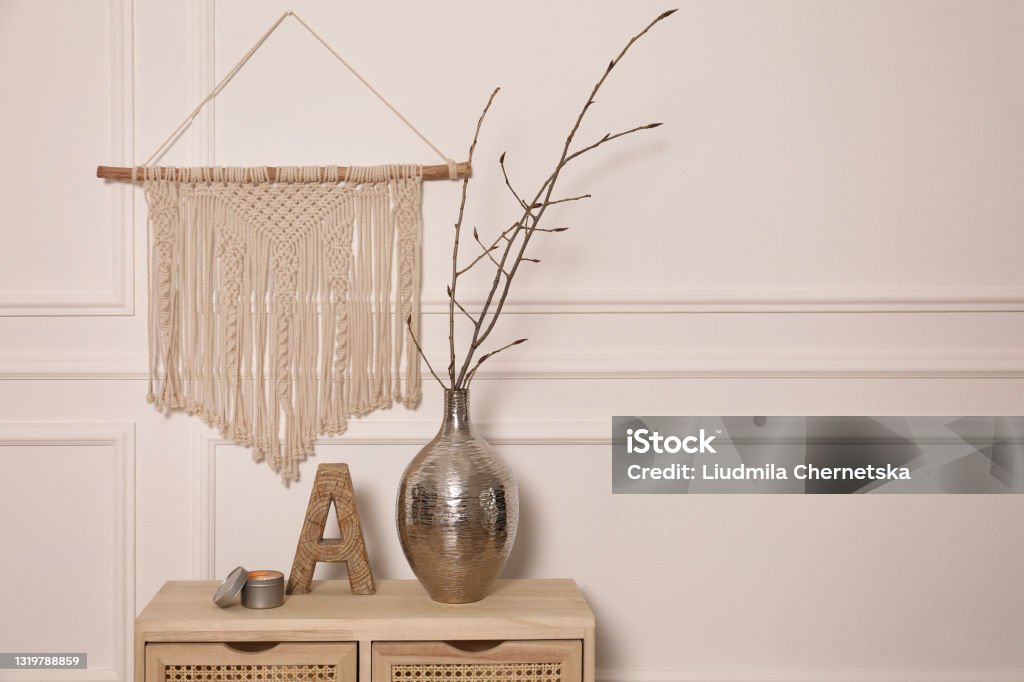 Tree twigs in metal vase and decor on wooden table near white wall. Space for text Indoors Stock Photo