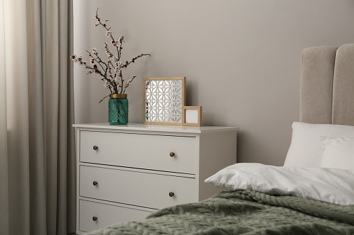Ramitas de árboles florecientes y decoración en cómoda blanca en el dormitorio photo