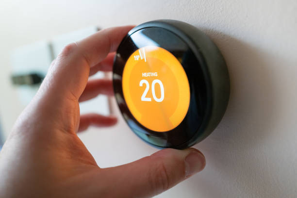Regulating heating temperature with a modern smart thermostat Man regulating heating temperature with a modern wireless thermostat installed on the wall at home. smart thermostat stock pictures, royalty-free photos & images