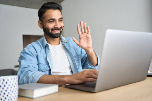 istock Young happy indian man waving hand having video call at home office using pc. 1319789974