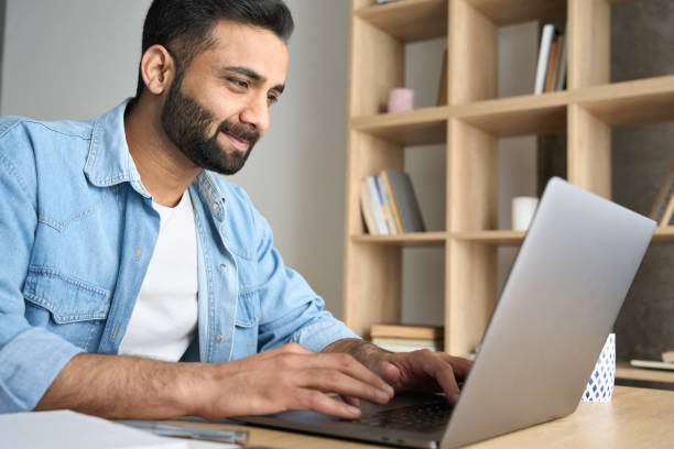 istock Young adult ethnic Hispanic businessman working from home office using laptop. 1319789978