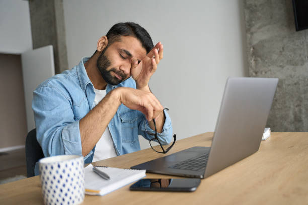 joven estudiante indio hispano cansado frotando los ojos sentado en el escritorio con computadora portátil. - agotamiento fotografías e imágenes de stock