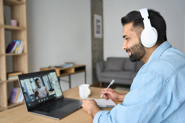 Indian latin male student having video call with male teacher on laptop. Latin indian adult student wearing headset having virtual meeting online call training educational webinar chatting with teacher at home office writing notes. Video e learning conference call on pc. video still stock pictures, royalty-free photos & images