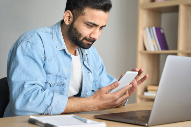 istock Young indian businessman works from home office using cellphone and laptop. 1319790020
