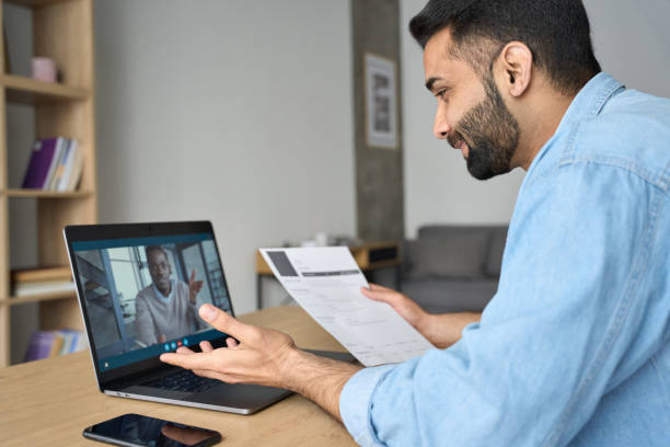 Young indian businessman having video call talking to potential employee. Young indian happy smiling businessman holding paper cv talking to male black man potential employee hiring for job. Virtual video call between employer and worker. Remote recruitment work concept. recruiter stock pictures, royalty-free photos & images