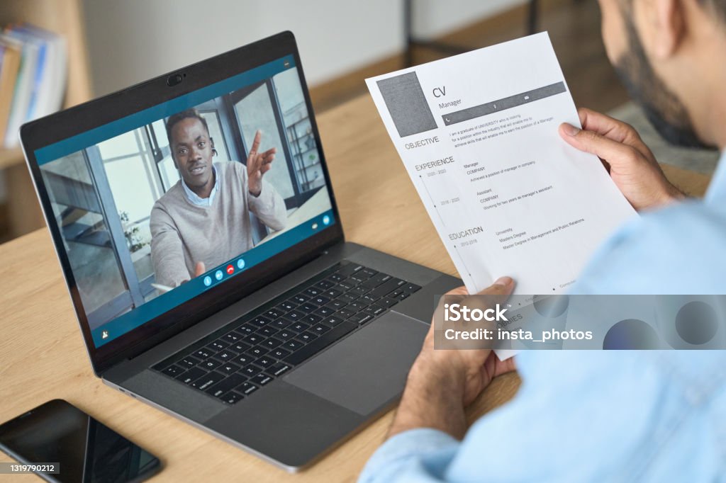 Young indian businessman having video call talking to potential employee. Young indian confident businessman holding cv talking to male black man potential employee hiring for job. Virtual video call between employer and manager worker. Remote recruitment work concept. Interview - Event Stock Photo