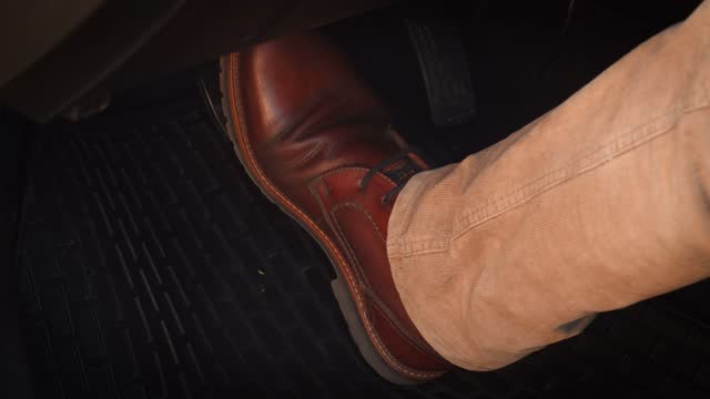 Man in brown shoes pressing the brake pedal in a modern car