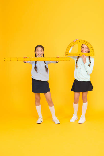 istock Learning school geometry. School children with measuring instruments on yellow background. Cute pupils holding protractor and ruler for school lesson. Small girls are back to school 1319791218
