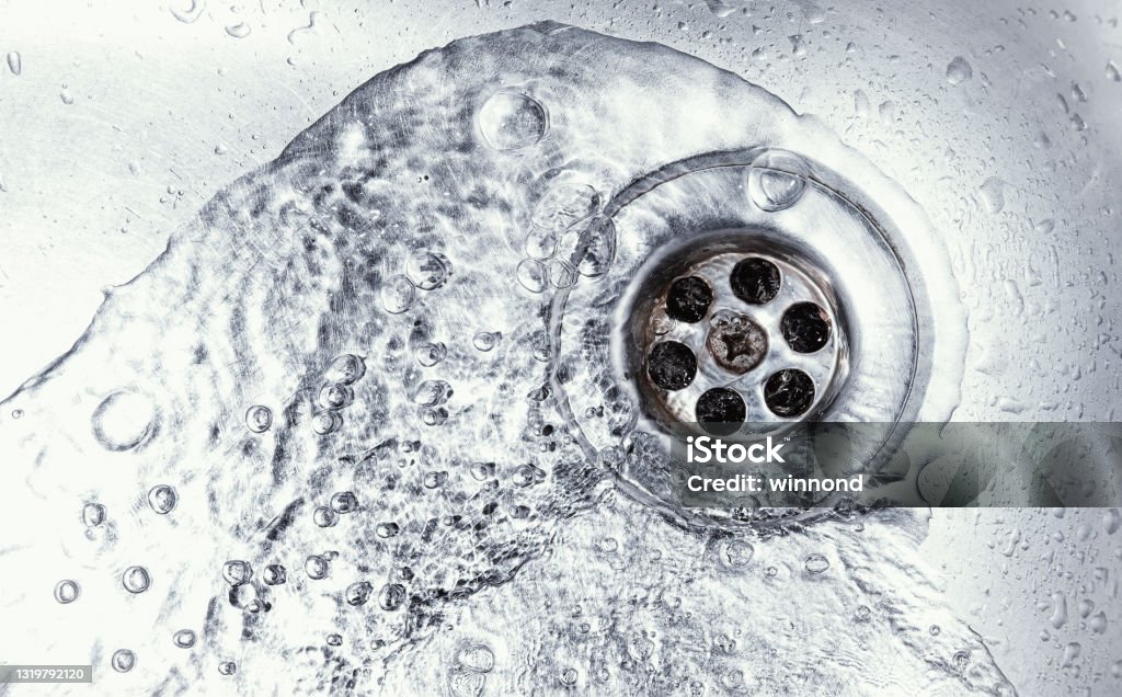 sink hole water drain down on stainless steel kitchen sink hole. top view sewer in washbasin. household plumbing. cleaning and hygiene concept. Sewer Stock Photo