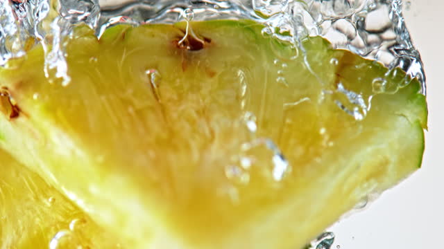 SLO MO LD Pineapple slices falling into water against white background