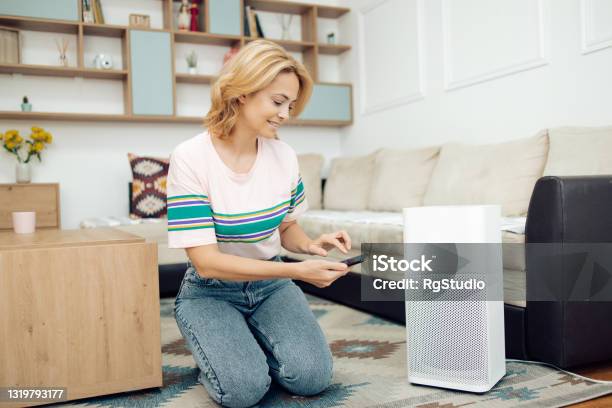 Woman Adjusting A Home Air Cleaner Using A Smart System Stock Photo - Download Image Now