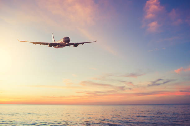 滑らかな波と日没の空の抽象的な背景を持つ熱帯のビーチの上を飛ぶ飛行機。 - landing sunset airplane flying ストックフォトと画像