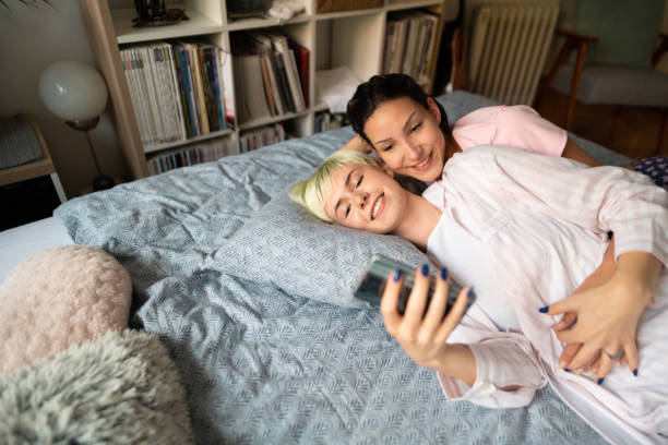 istock Smiling lesbian couple lying in bed and using a smartphone together 1319800222