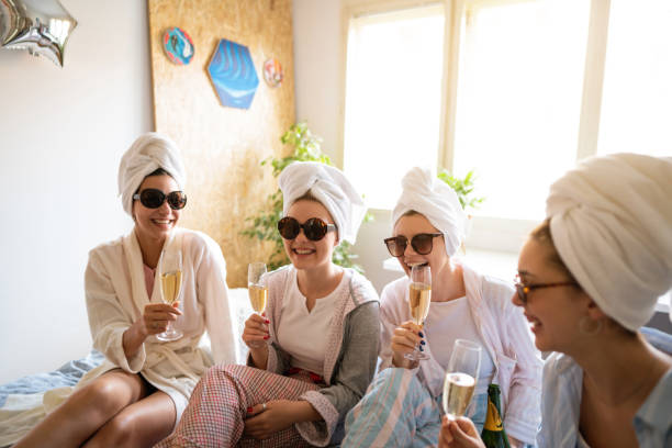 Smiling young women talking and drinking champagne at a slumber party Four young Caucasian women with towels and sunglasses having fun together at the slumber party while talking and  drinking champagne. bachelorette party stock pictures, royalty-free photos & images