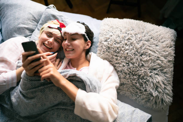 istock High-angle view of two smiling young women with sleeping masks lying together in bed while looking at the phone 1319801170