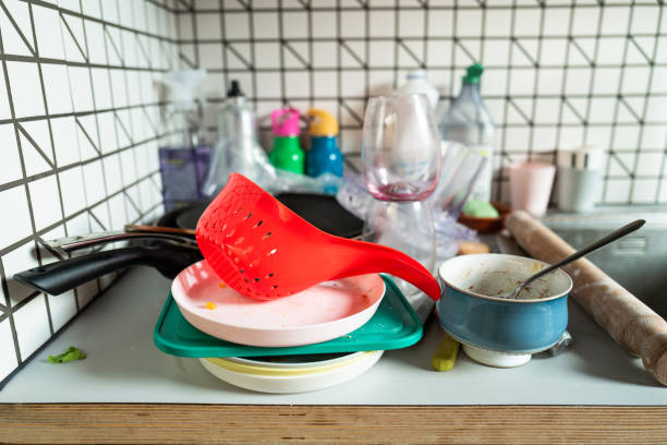 A pile of dirty dishes, including plates, pots and pans and other dirty kitchen appliances stacked in the kitchen next to the sink.