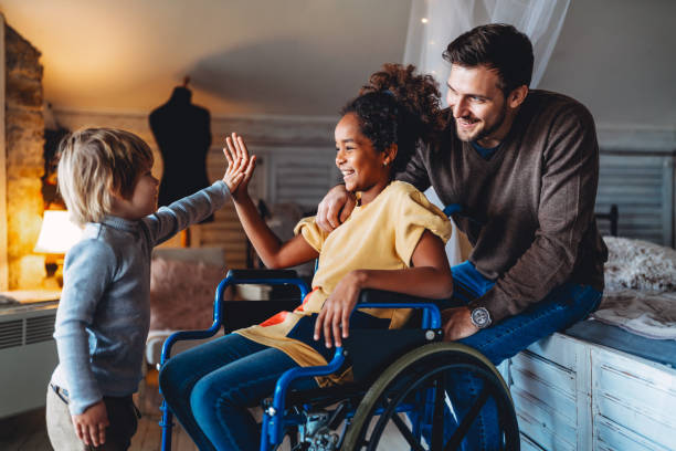 buona famiglia multietnica. bambina sorridente con disabilità in sedia a rotelle a casa - multi ethnic family foto e immagini stock