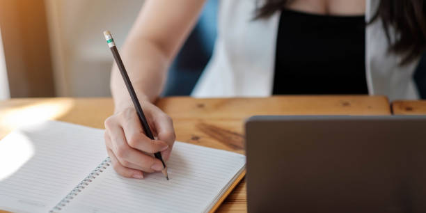 istock Close up woman's hands with laptop computer, notebook and pen taking notes in business office 1319811083