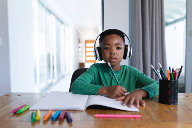 istock African american boy in online school class, using headphones and writing in his notebook 1319812142