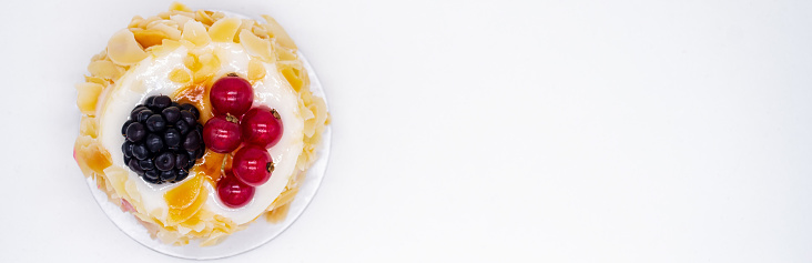 Banner with cream cake, almond petals, red currants and blackberries. Concept of holiday, birthday, sweet tooth. White background. Copy space.