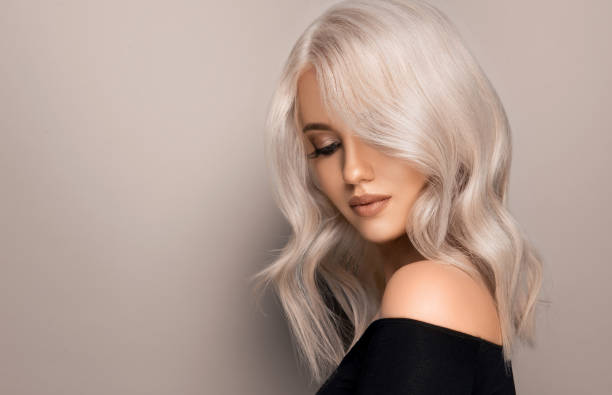 bonita cara de mujer joven en maquillaje glamuroso está rodeando mechones rizados de pelo rubio. peluquería, coloración de cabello y maquillaje.. - leonado fotografías e imágenes de stock